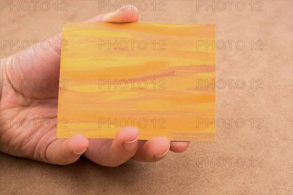 Hand holding painted note paper on brown background