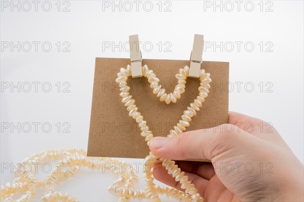 Pearl necklace forms heart shape on paper on white background