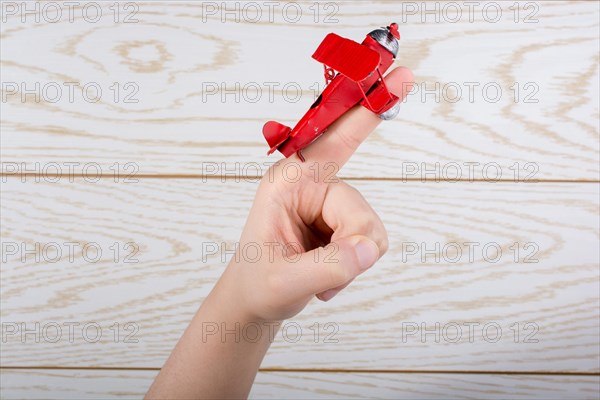 Hand holding a red toy plane on a on wooden texture