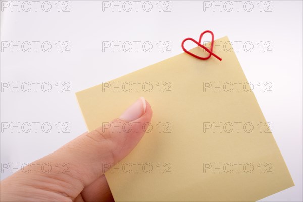 Hand holding a notepaper heart shaped clip on a white background