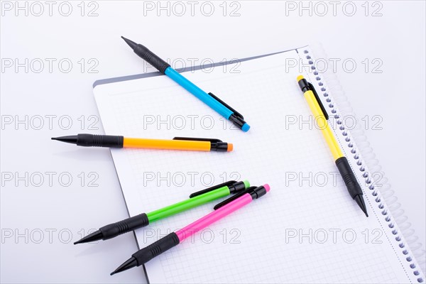 Mechanical pencils of various color on a notebook on white background