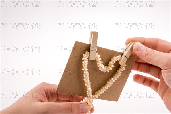 Pearl necklace forms heart shape on paper on white background