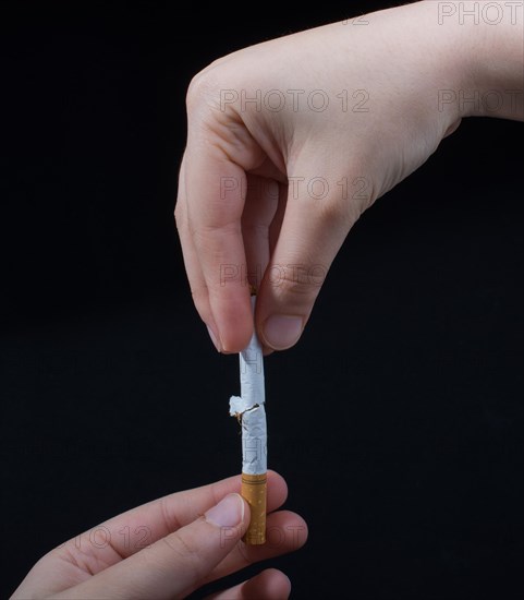 Hand is breaking a cigarette on a black background