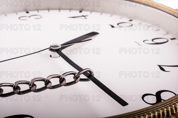 Chain tied to minute hand of a clock and pulled on a white background