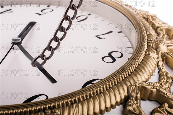 Chain tied to minute hand of a clock and pulled on a white background