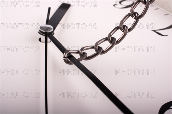 Chain tied to minute hand of a clock and pulled on a white background