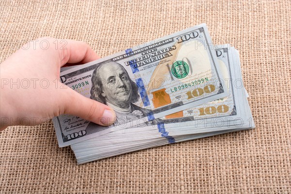 Hand holding banknote bundle of US dollar on a linen canvas background