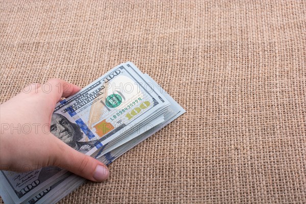 Hand holding banknote bundle of US dollar on a linen canvas background