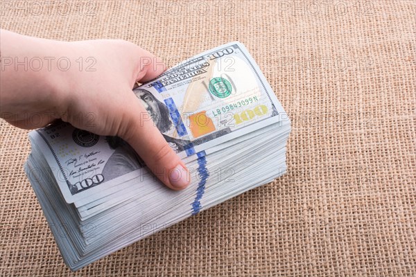 Hand holding banknote bundle of US dollar on a linen canvas background