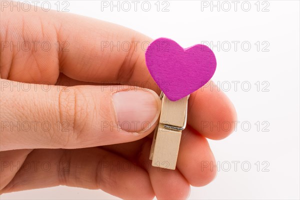 Hand holding a red clothespin with a heartshape on a white background