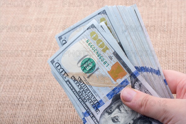 Hand holding banknote bundle of US dollar on a linen canvas background