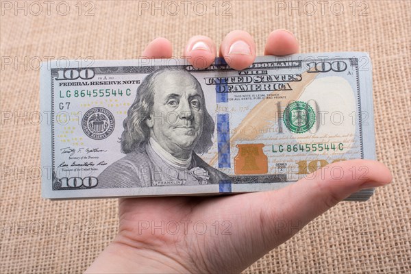 Hand holding banknote bundle of US dollar on a linen canvas background