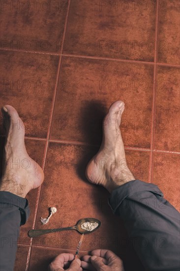 Top view of a man sitting barefoot on the floor with a heroin syringe in his hand Concept of drug addiction