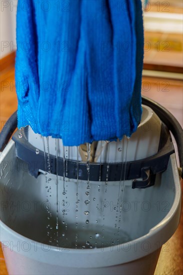 Close-up of a blue mop dripping drops of water into its bucket