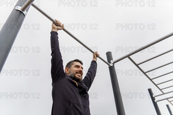 Young man dressed in black training on a pull-up bar in an outdoor gym