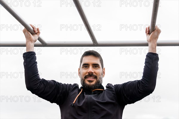 Young man dressed in black training on a pull-up bar in an outdoor gym