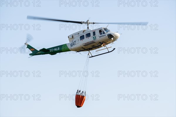 Firefighting helicopter in mid-flight dropping water bag on flames