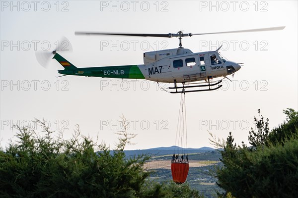 Firefighting helicopter in mid-flight dropping water bag on flames