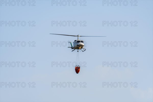 Firefighting helicopter in mid-flight dropping water bag on flames