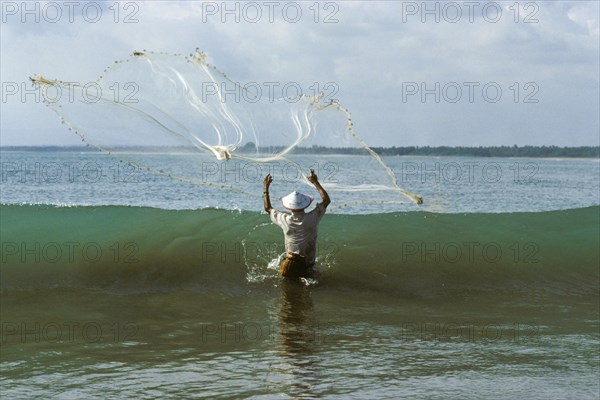 Fisherman with cast net in front of wave