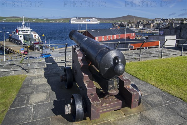 Cannon at 17th century Fort Charlotte in the centre of Lerwick and cruise ship in the Bressay Sound