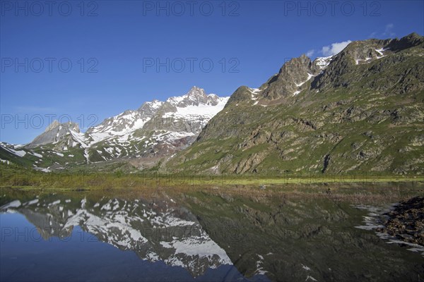 Reflection of mountains of the Mont Blanc massif and the Limestone Pyramids in water of Lago Combal lake in Val Veny in the Italian Alps