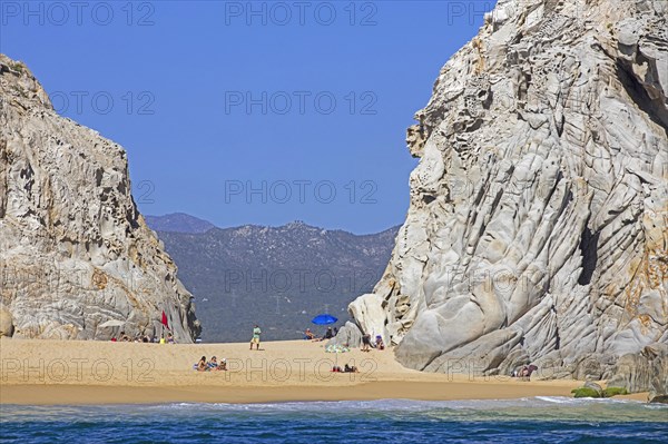 Limestone sea cliffs and tourists sunbathing on secluded beach near the seaside resort Cabo San Lucas on the peninsula of Baja California Sur