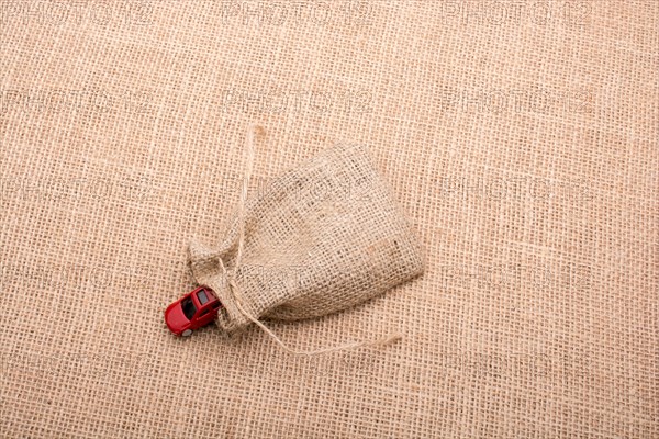 Red toy car coming out of a linen sack on a linen canvas