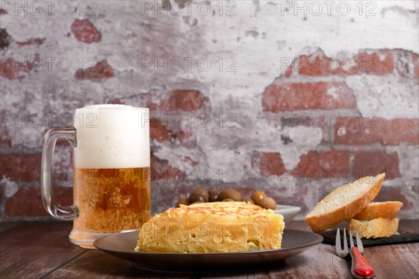 Typical spanish potato omelette freshly made on a wooden table with a fresh pitcher of beer