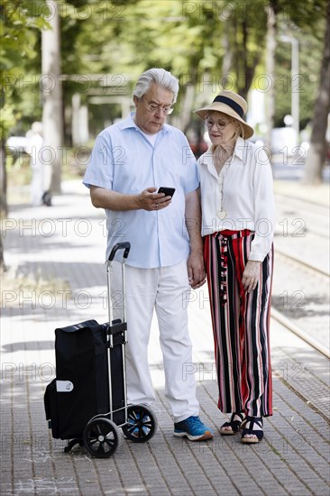 Elderly couple waiting for the tram at a stop with a smartphone in hand