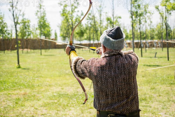 Archer with bow in traditional clothes shooting an arrow