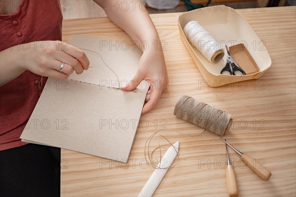 Close-up detail of woman's hands sewing a handmade notebook made in her workshop