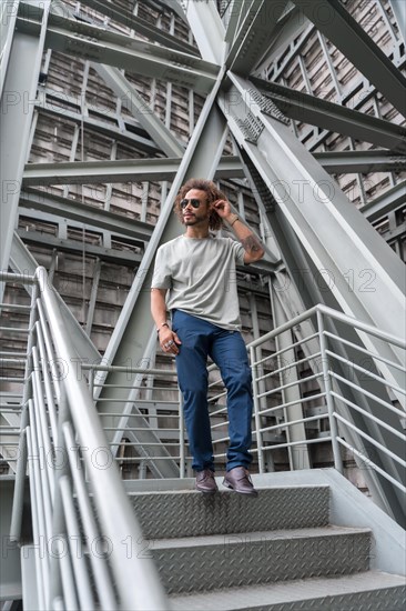 Young man with afro hair wearing sunglasses walking down the stairs in the city