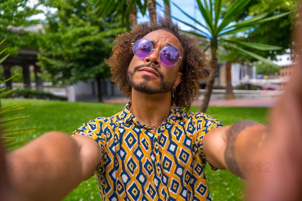 Afro-haired man on summer vacation next to some palm trees next to the beach taking a selfie with both hands. Travel and tourism concept