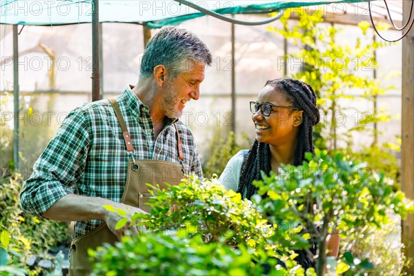 Master gardener teaching schoolgirl flower nursery in greenhouse smiling