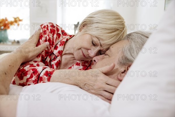 Elderly couple lying together in bed in bedroom embracing tenderly