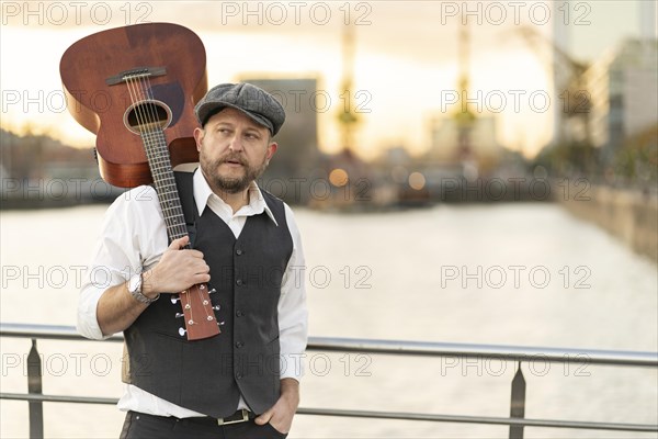 Guitarist posing on a bridge over a river with his guitar