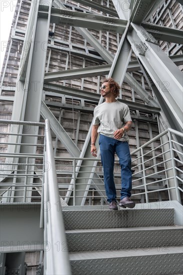 Young man with afro hair wearing sunglasses walking down the stairs in the city
