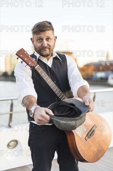 A street musician looking at camera and carrying his guitar while asking for tips