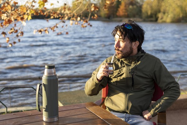 Latin man enjoying the sunset at the river while drinking mate