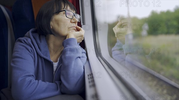 Elderly lady in glasses travels in train and looking out the window reflected in the glass