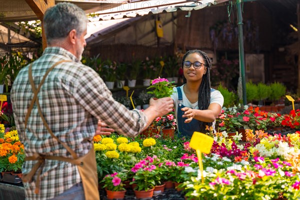 Female customer buying flowers from a gardener in a nursery inside the greenhouse