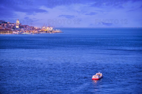 Night view of Lisbon over Tagus river from Almada with ferry and tourist boat in evening twilight. Lisbon