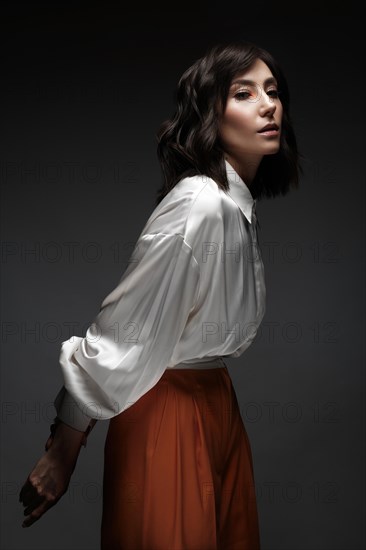 Spectacular beautiful woman in a trendy orange suit with classic make-up. Beauty face. Photo taken in the studio on a white background