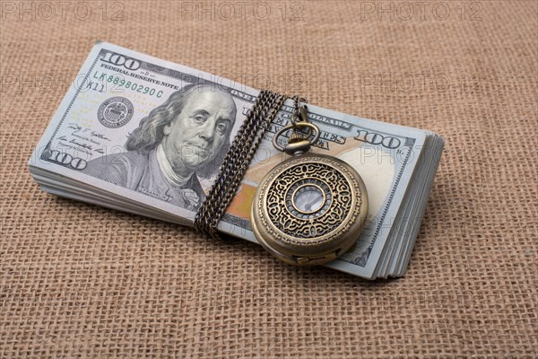 Pocket watch wrapped around banknote bundle of US dollar
