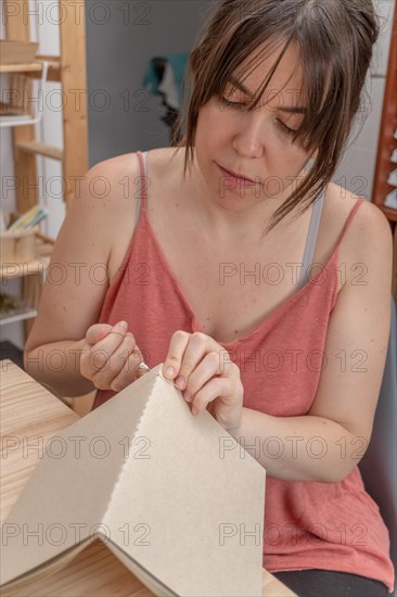 Young brunette girl with long hair craftswoman working on her products in her home workshop sewing notebooks