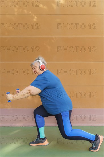 White haired obese older woman exercising with dumbbells and headphones listening to music for weight loss .isolated on orange background and copy space