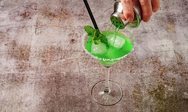 Hand of a woman serving a mint cocktail with ice straw and mint leaves with a cocktail shaker