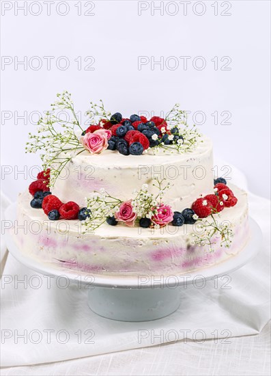 Summery fresh two tier wedding cake decorated with berries and flowers festive cream cake on light background