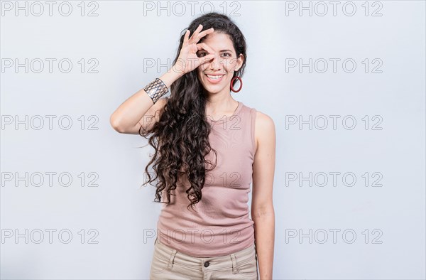 Happy young girl making ok gesture with hand looking through fingers. Friendly girl doing ok gesture looking through fingers